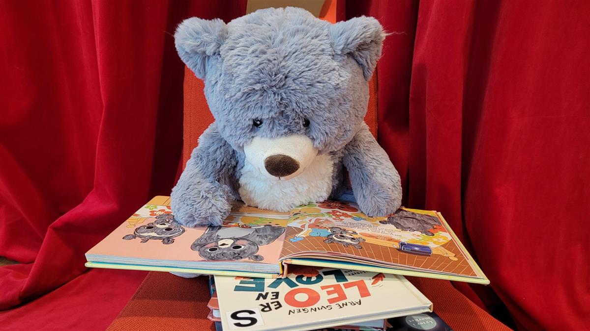 En kosebamse sitter og leser barnebøker. Foto - Klikk for stort bilde