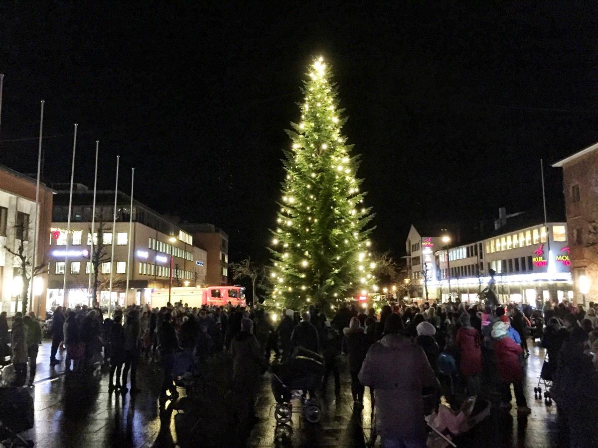 Folk samler seg foran en julegran i mørket - Klikk for stort bilde