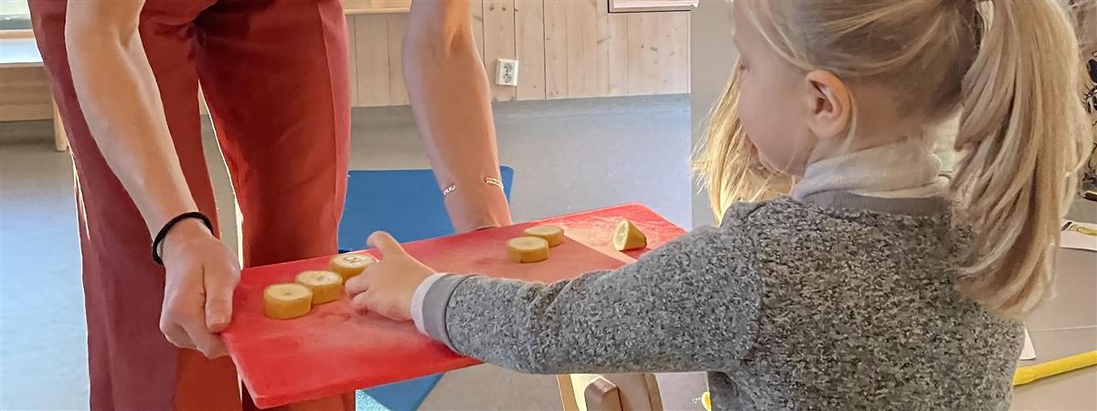 En liten jente tar en bananbit fra et serverringsfat. Foto - Klikk for stort bilde